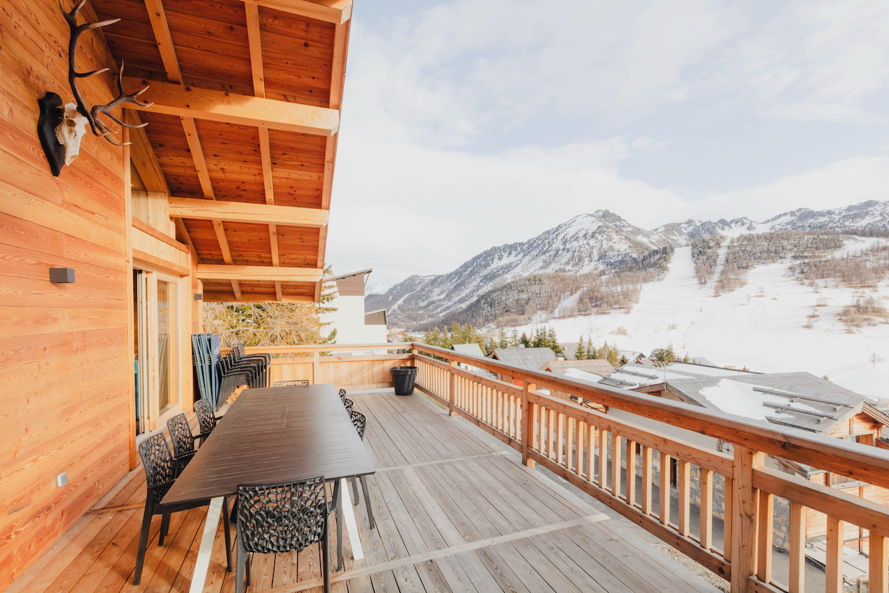 Terrasse en bois du chalet avec table, chaises et vue sur les pistes enneigées