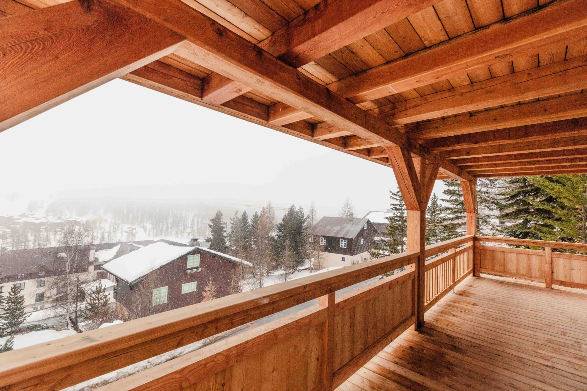 Balcon couvert en bois du chalet avec vue sur le village sous la neige