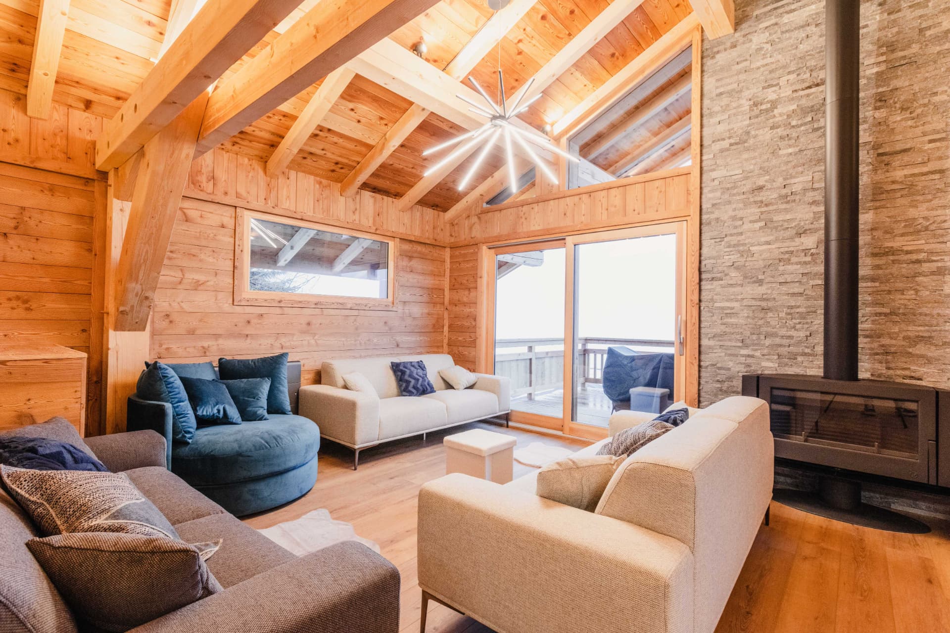 Salon du chalet avec poêle à bois, canapés et accès terrasse