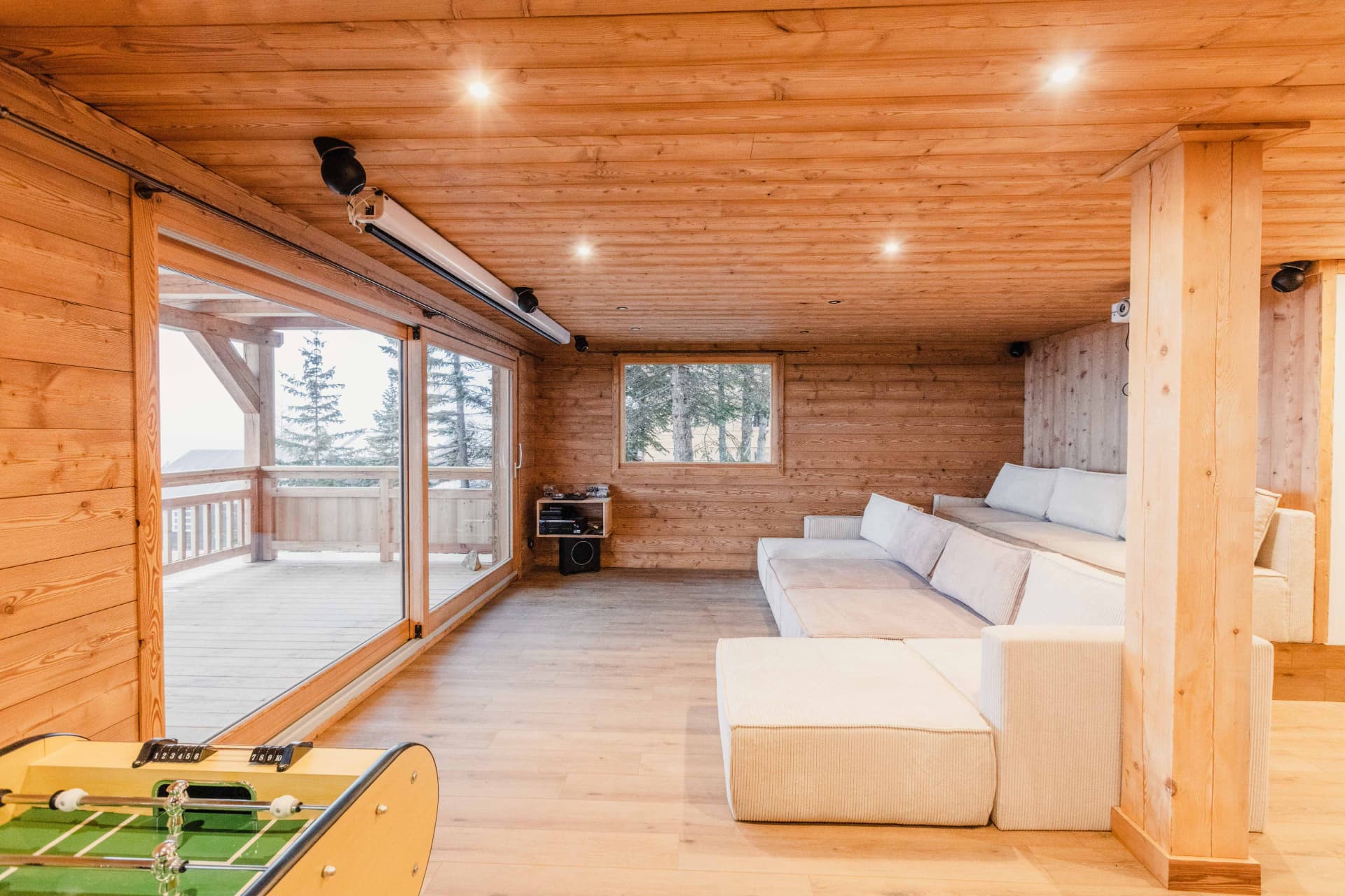 Salle de détente avec grand canapé, baby-foot et baie vitrée sur la terrasse